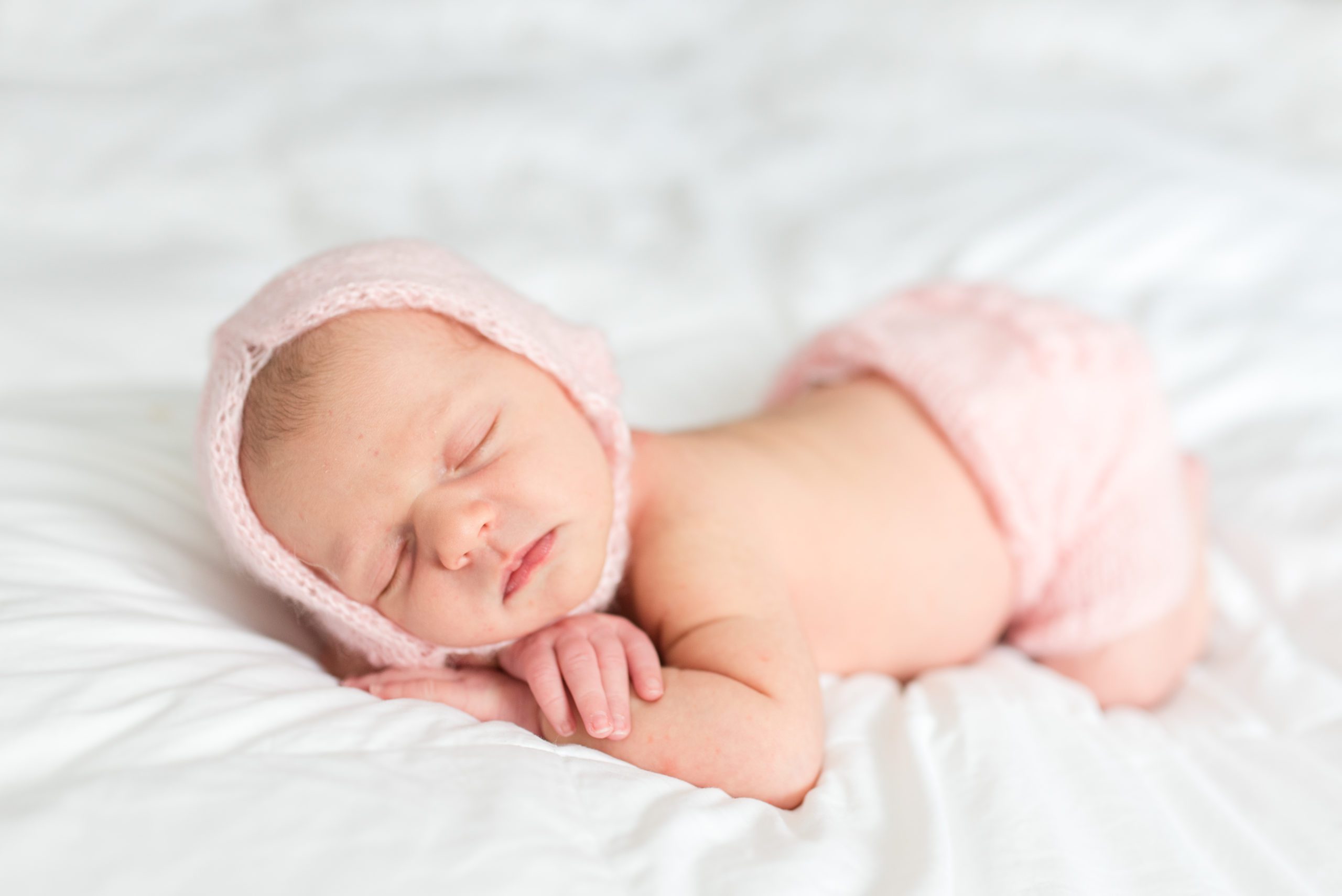 Annessa as a newborn sleeping on the bed with cute bonnet