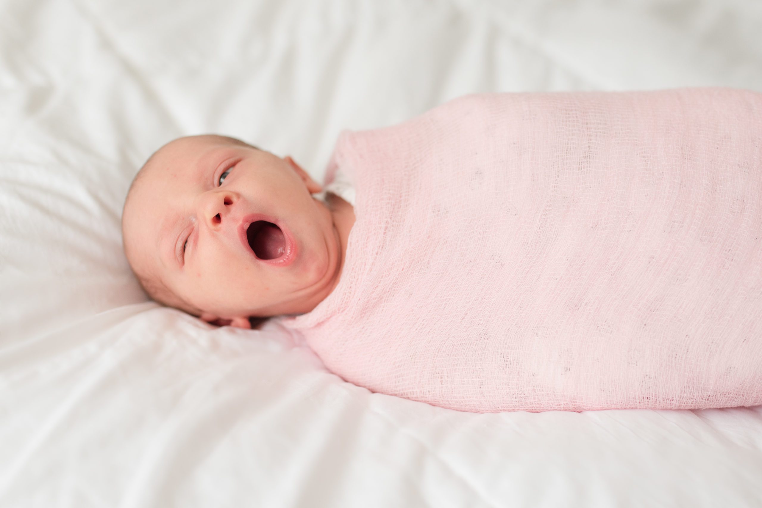 Annessa as a newborn sleeping on the bed wrapped in pink swaddle