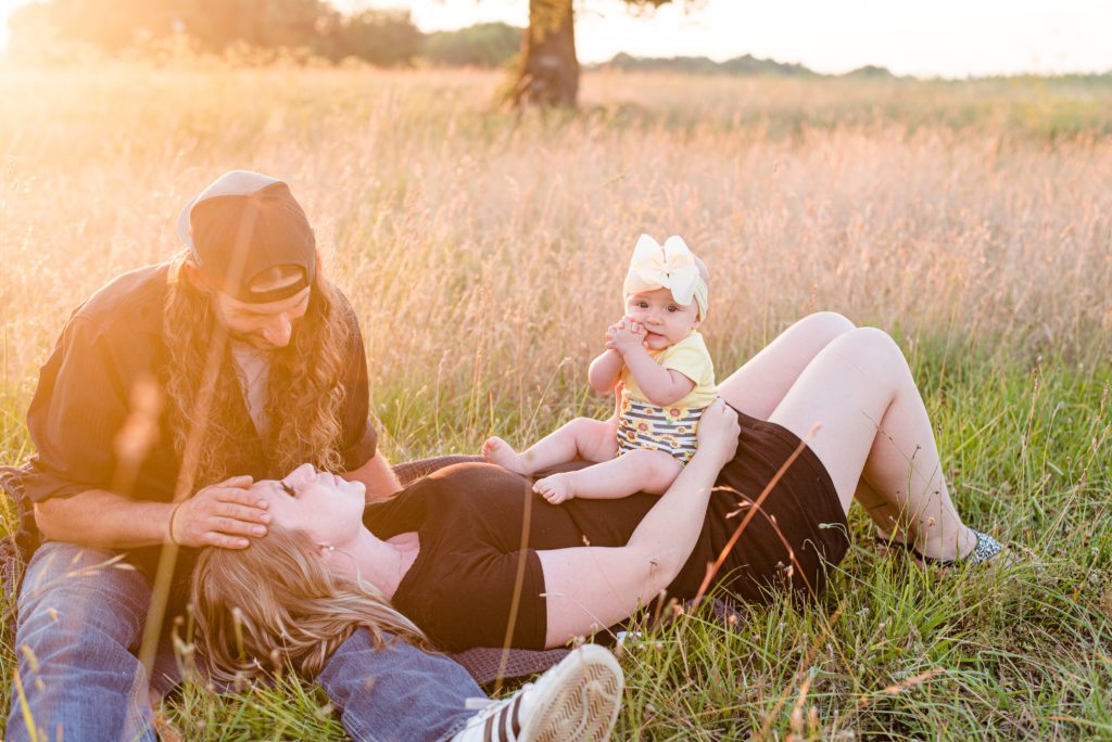 6 month old Annessa with her parents laying in a field at sunset