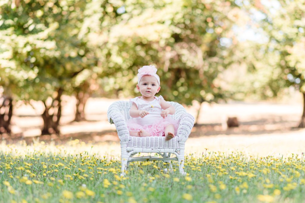 Annessa at 9 months sitting in a white rocking chair in a field