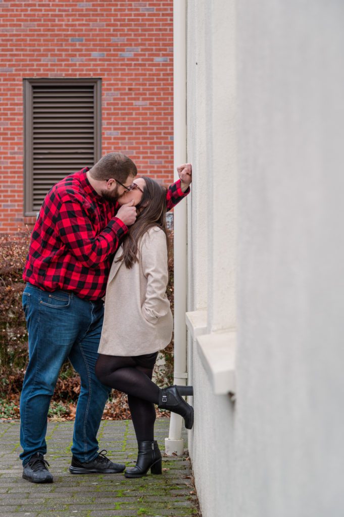 Engaged couple kissing against wall at Lewis and Clark College