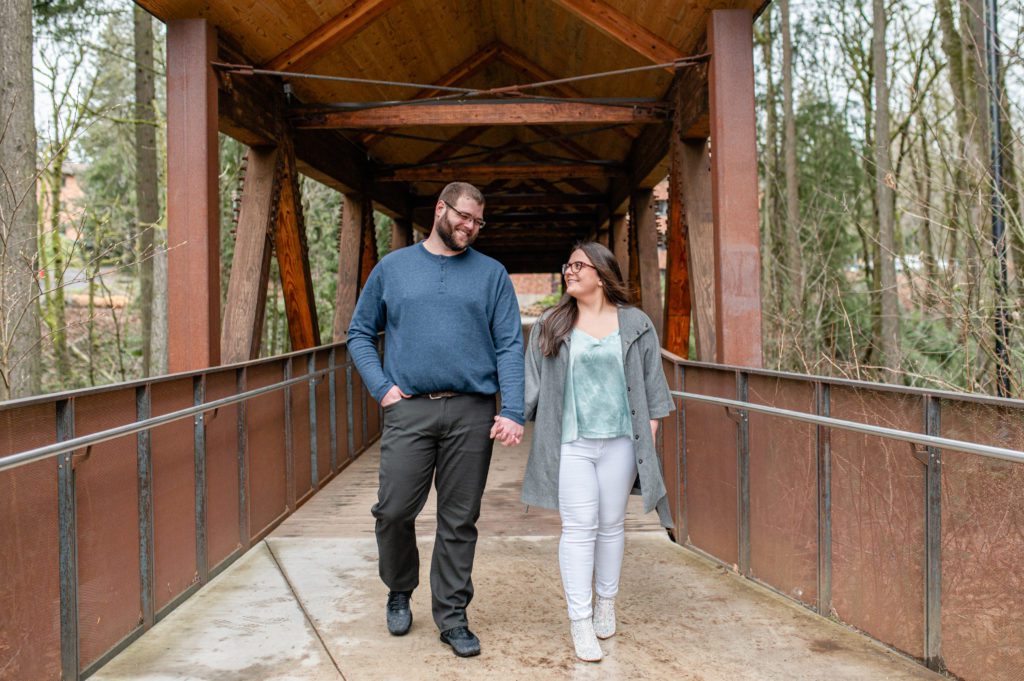 Engaged couple walking and holding hands under covered bridge