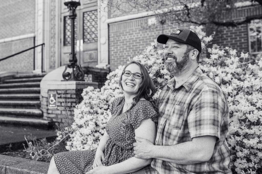 Engaged couple sitting in front of flowers laughing