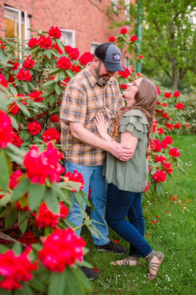 Engaged couple looking at each other in the red flower bushes