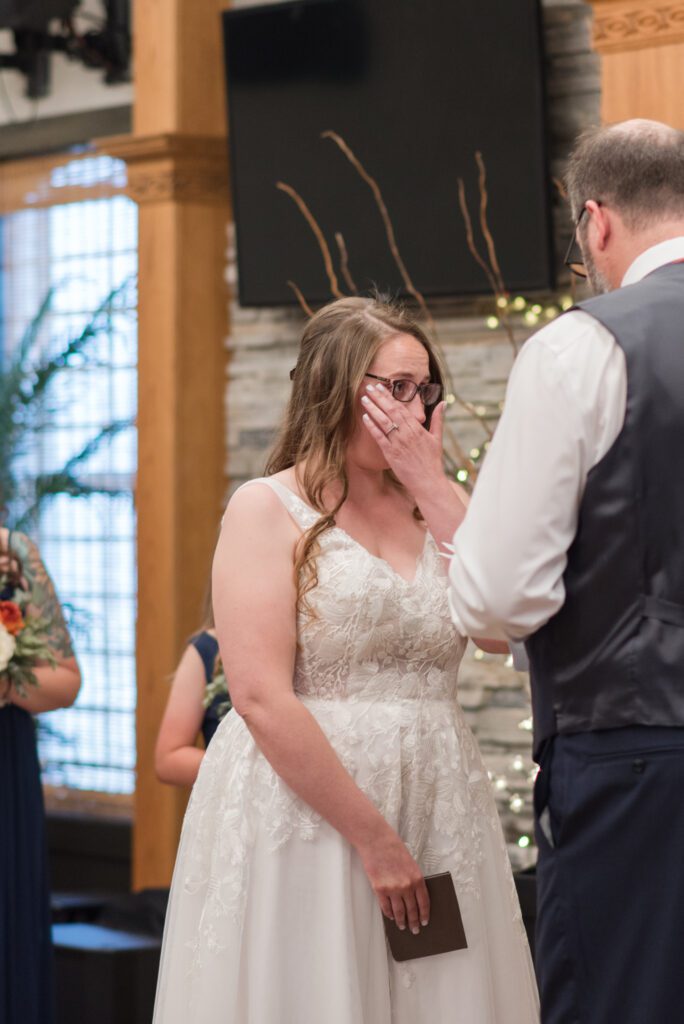 Bride wiping tear from her eye during her husbands vows at their wedding ceremony in Oreogn