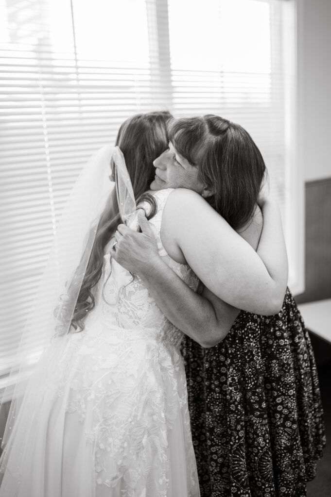 Bride and her mother hugging after she helps her into her dress