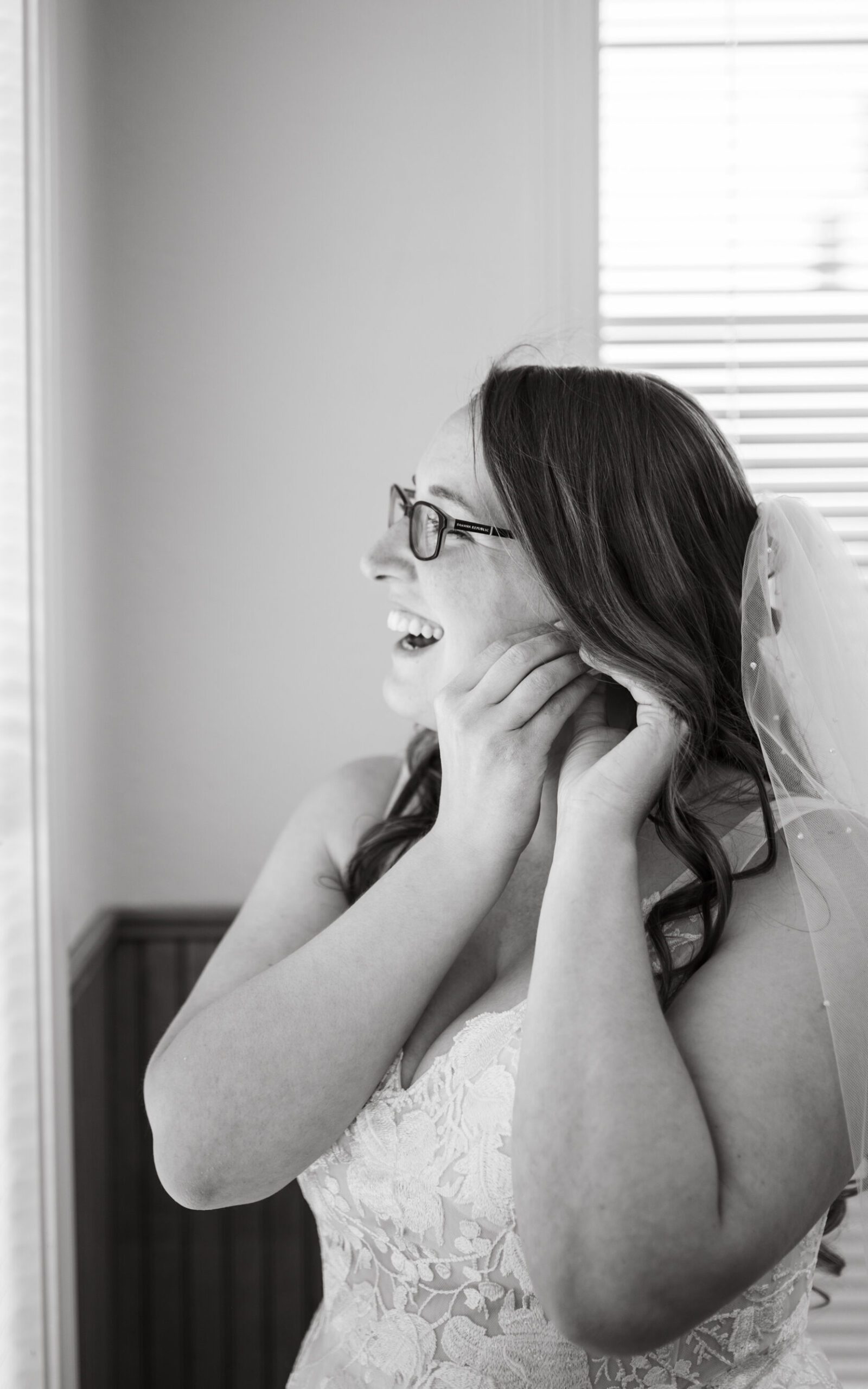 Bridal portrait where the bride is putting her earrings on as she looks out the window