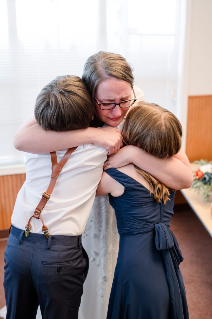 Bride and children first look in wedding dress hugging and crying