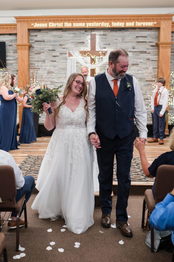 Bride and groom walking down the aisle together after getting married in Oregon as the groom grabs his moms hand as she congratulates him