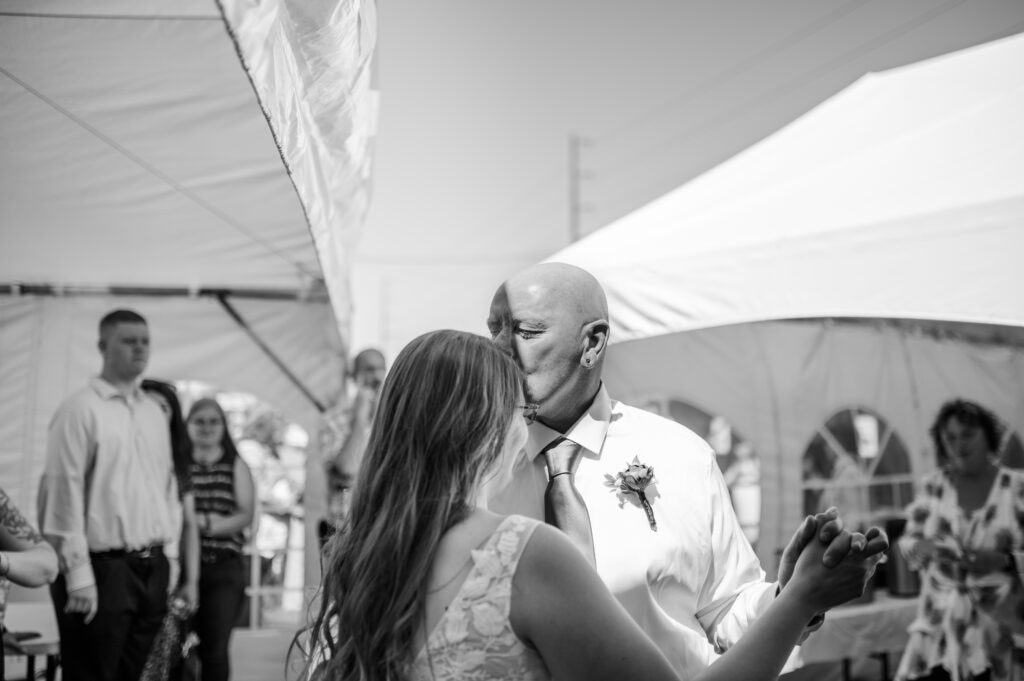 Father daughter first dance while father kisses his daughter on the forehead