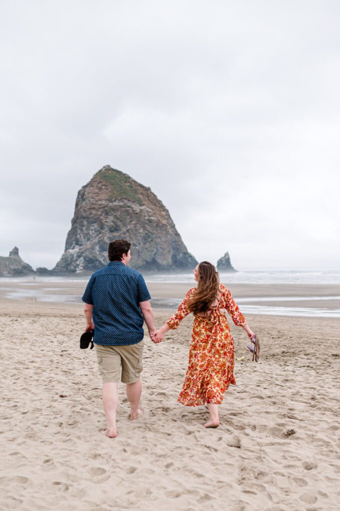 Couple walking towards Haystack Rock in Cannon Beach Oregon during their engagement session