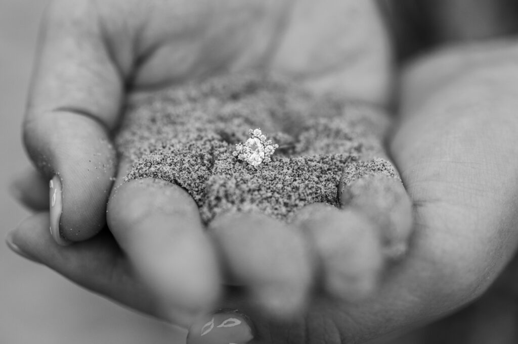 Bride holding sand in her hand with her ring on top during their engagement session at Cannon Beach in Oregon