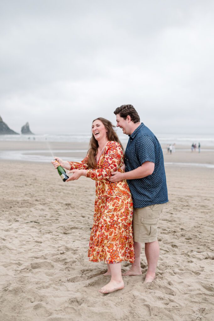 Bride laughing while she pops champagne during engagement session at cannon Beach, OR