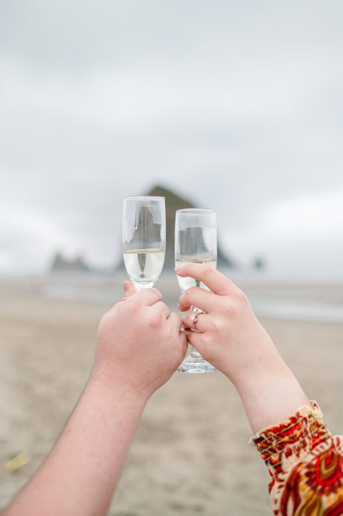 close up of champagne glasses clinking together in front of haystack rock in cannon beach oregon