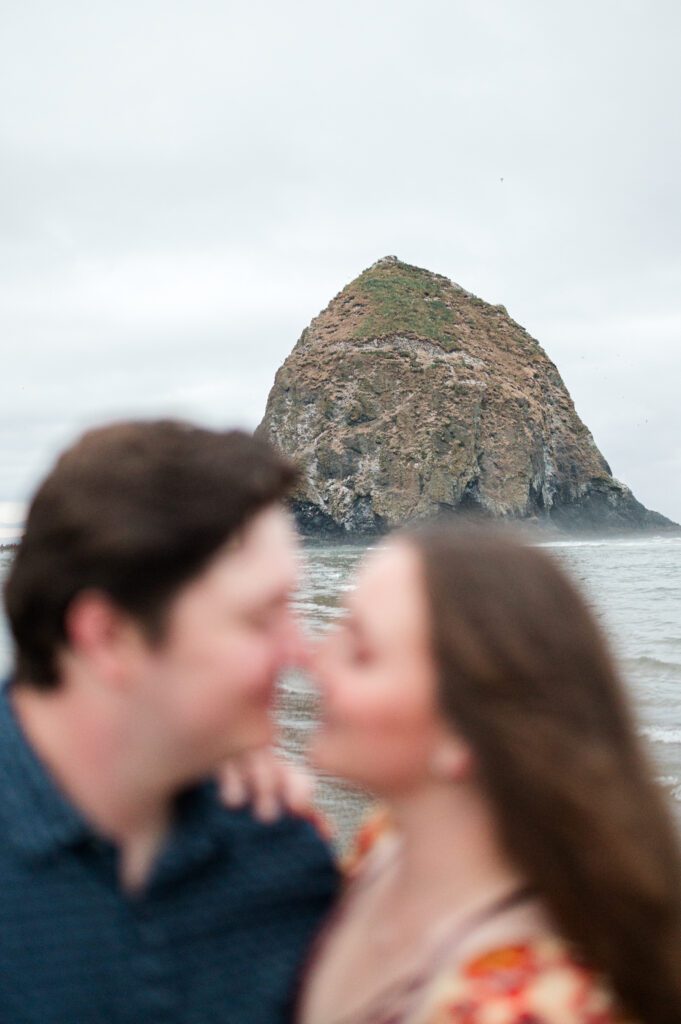 haystack rock with the engaged couple in the foreground in cannon beach oregon