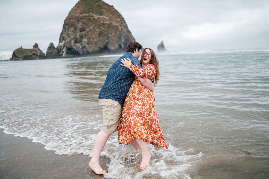 groom about to push bride in water during their engagement session at cannon beach oregon