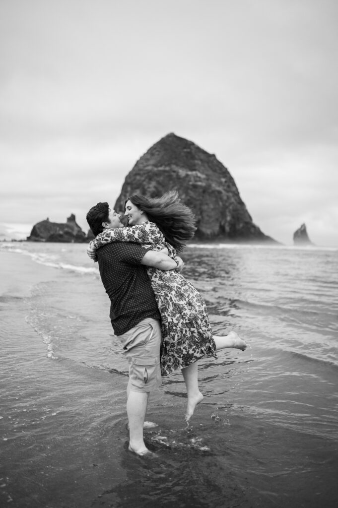 black and white image of engaged couple spinning in the water in cannon beach oregon