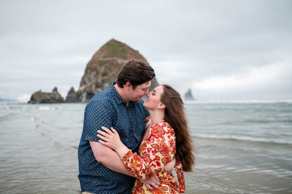 couple about to kiss in front of haystack rock in cannon beach oregon for their engagement session